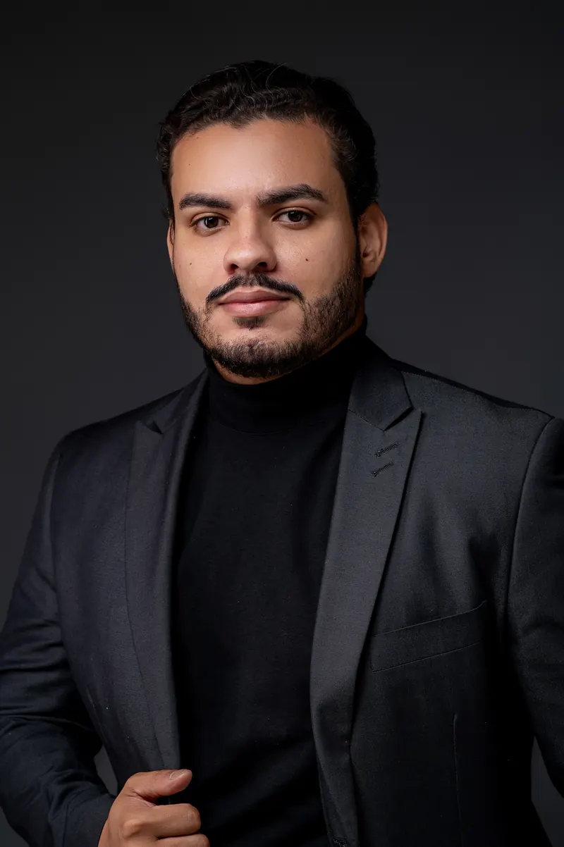 Angelo Gramlich, de gola alta preta e blazer escuro, olhando para a câmera